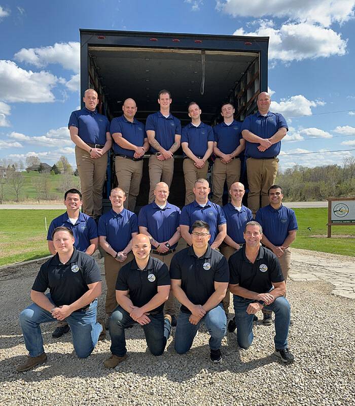 Group in navy short sleeve polo shirts standing and kneeling in three levels at the back of their moving truck