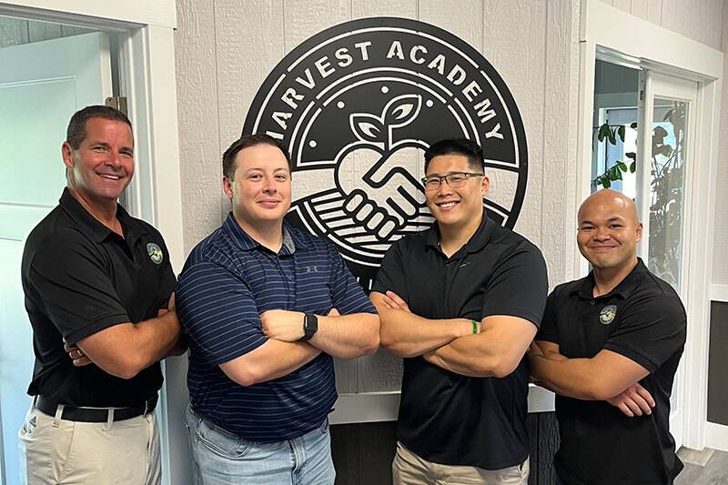 The four men who make up the Harvest Academy leadership group standing in front of a black iron Harvest Academy sign with their arms crossed